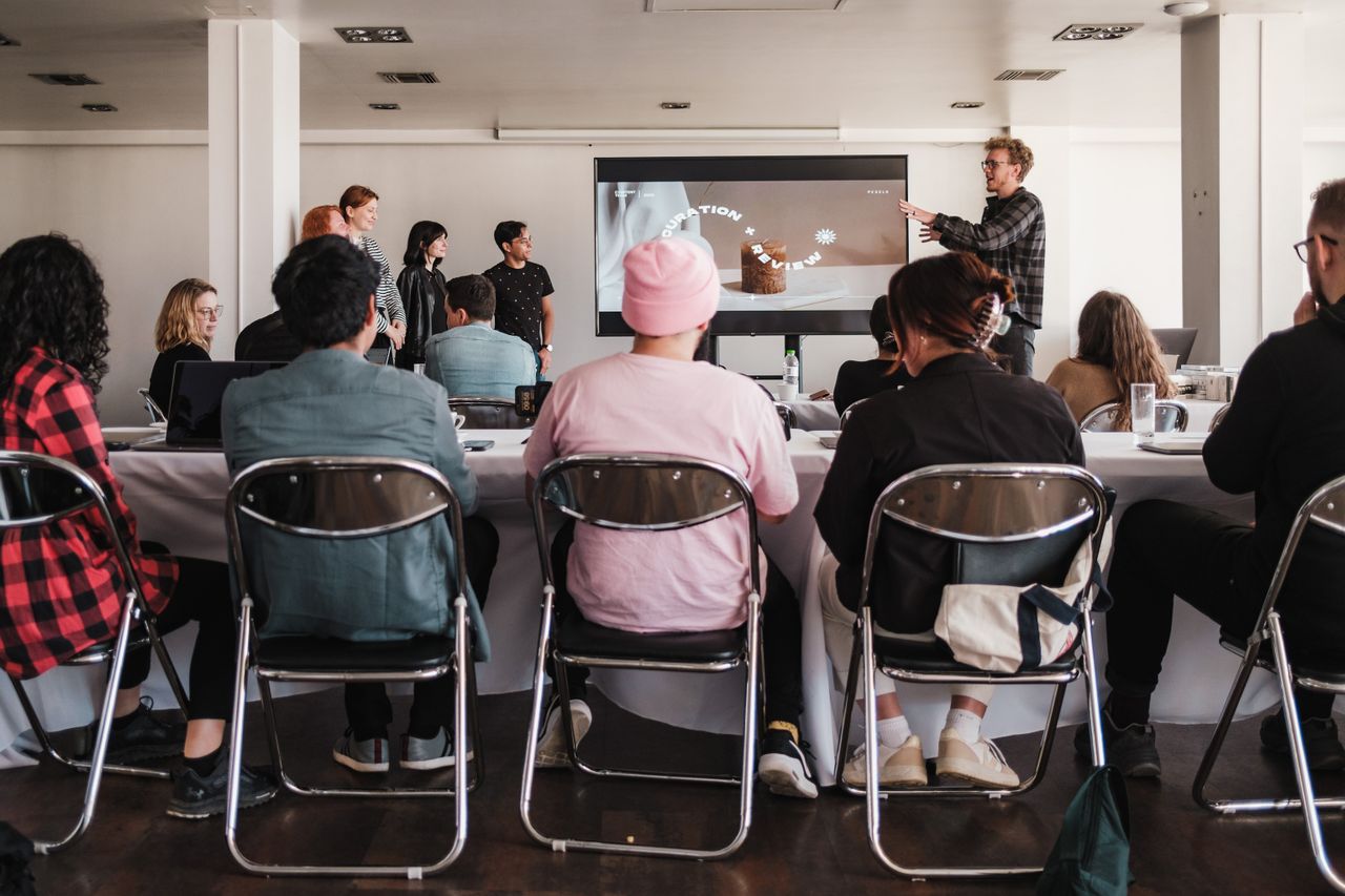 Une salle de réunion où une quinzaine de personnes assises à des tables écoutent une intervenante devant un écran de projection.