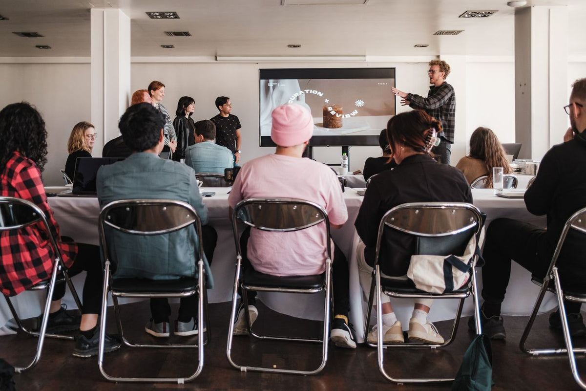Une salle de réunion où une quinzaine de personnes assises à des tables écoutent une intervenante devant un écran de projection.
