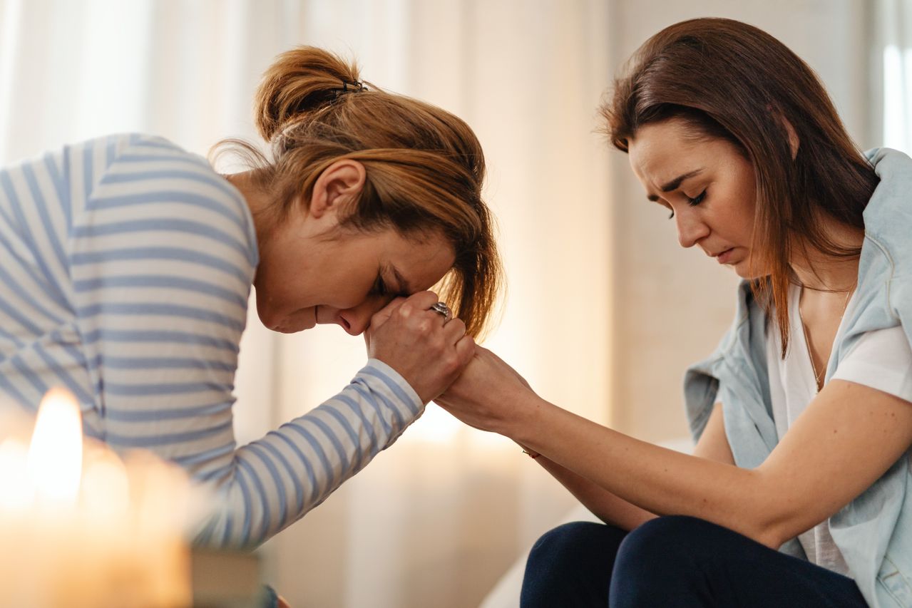 Deux femmes assises côte à côte, l'une penchée en avant le front contre ses mains jointes, l'autre le regard baissé.