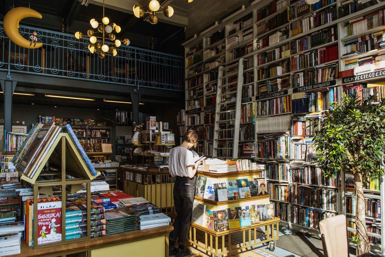L'intérieur d'une grande librairie sur deux niveaux, des rayonnages du sol au plafond, une personne seule devant un présentoir.