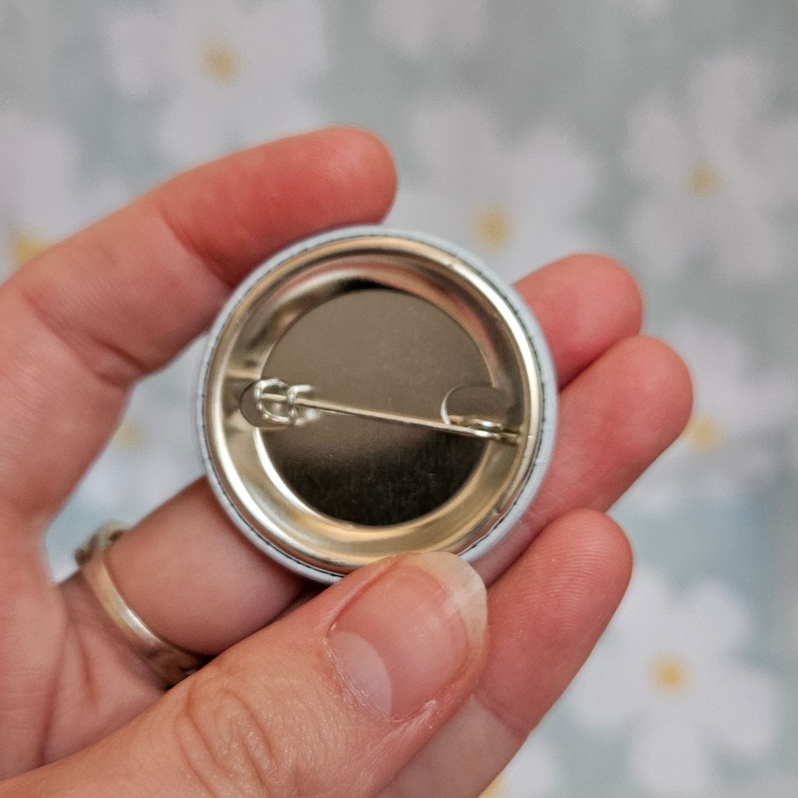 Dos métallique du badge de 38 mm, tenu dans une main, montrant l'épingle de fixation