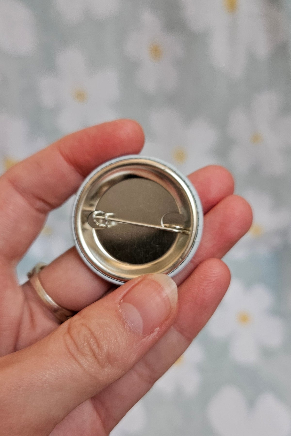 Dos métallique du badge de 38 mm, tenu dans une main, montrant l'épingle de fixation