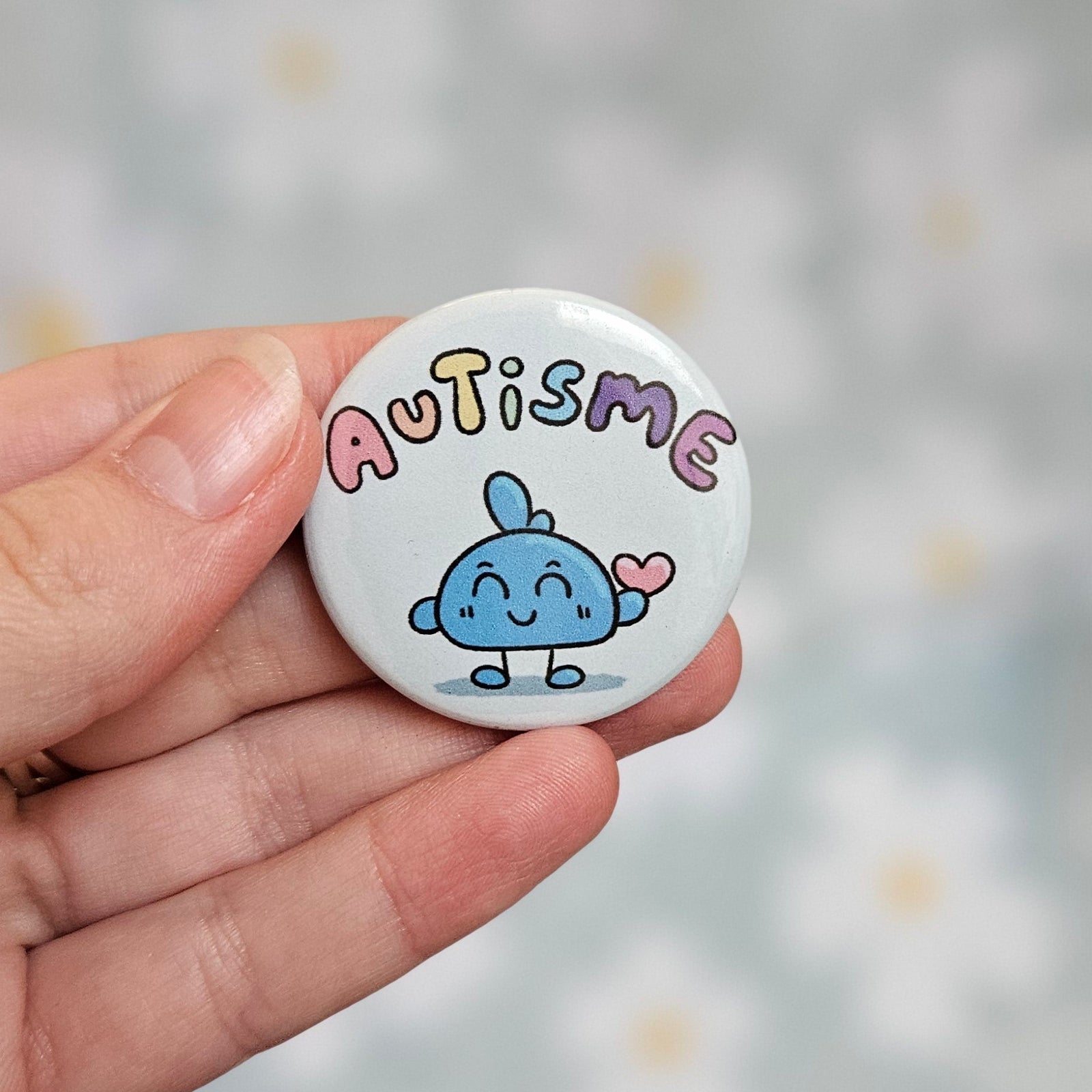 Badge rond de 38 mm portant le mot autisme, en teintes pastel