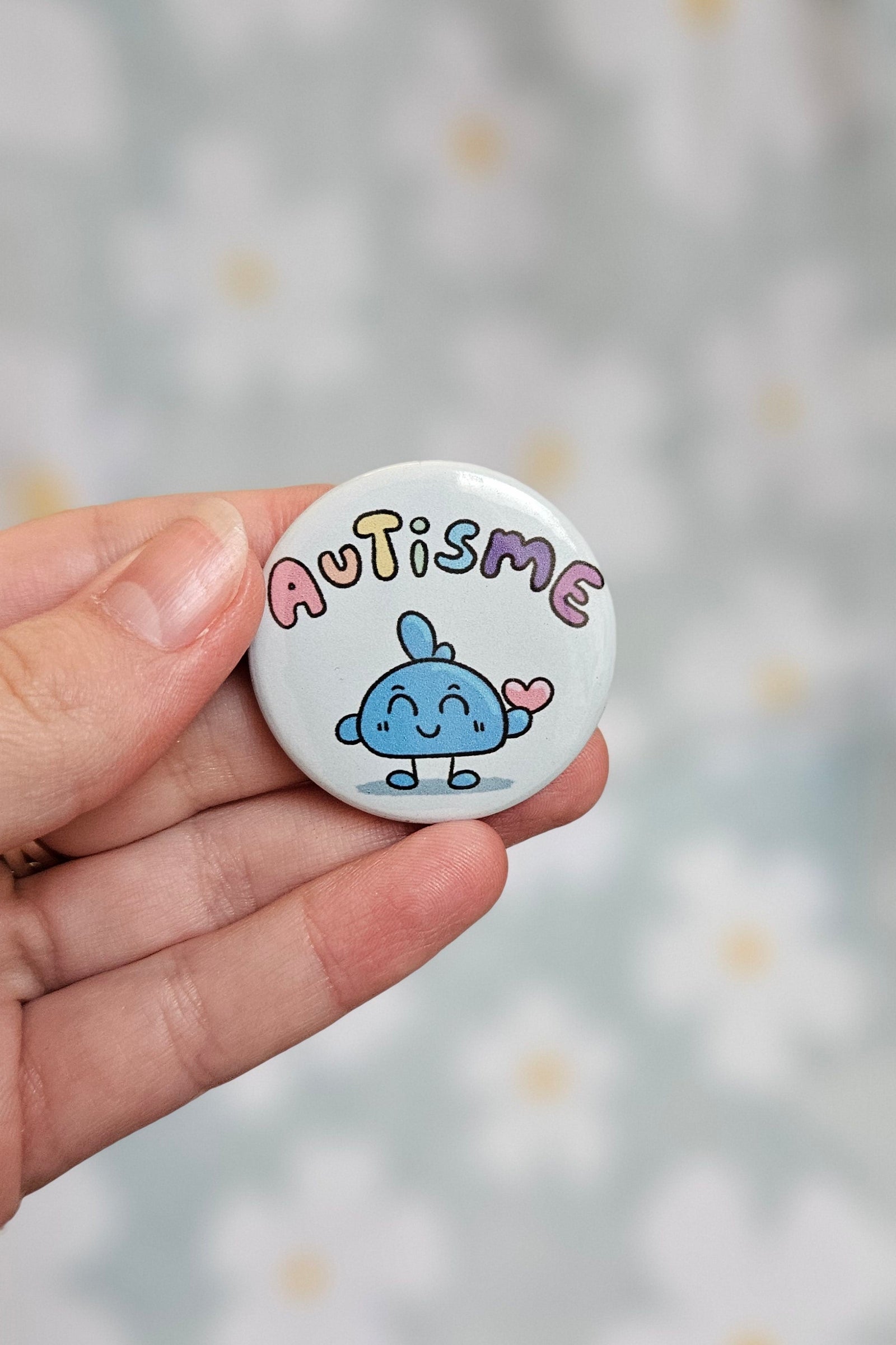 Badge rond de 38 mm portant le mot autisme, en teintes pastel