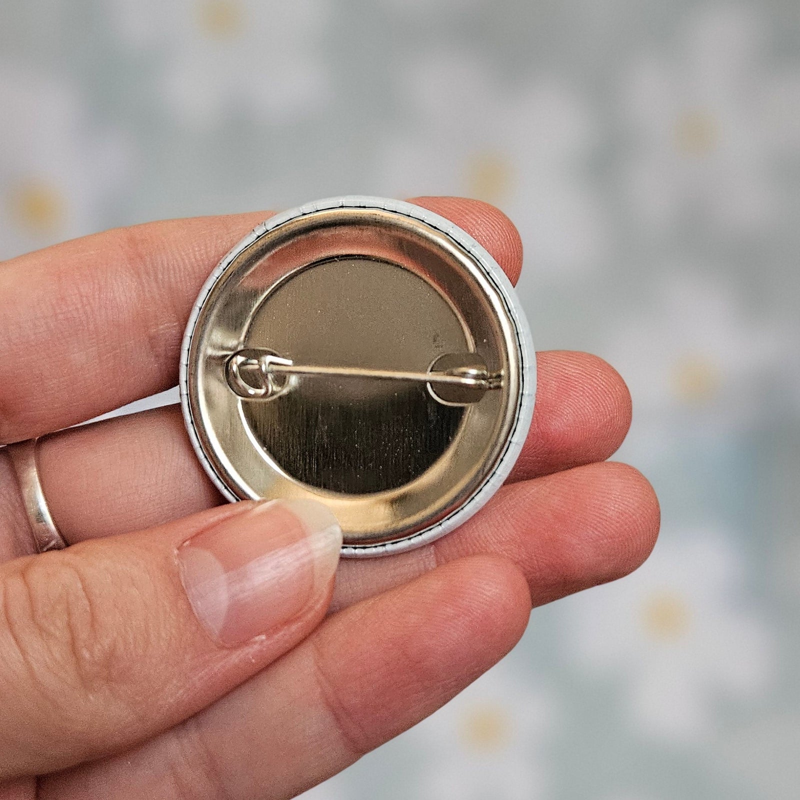 Dos métallique du badge autisme de 38 mm, tenu dans une main, montrant l'épingle de fixation