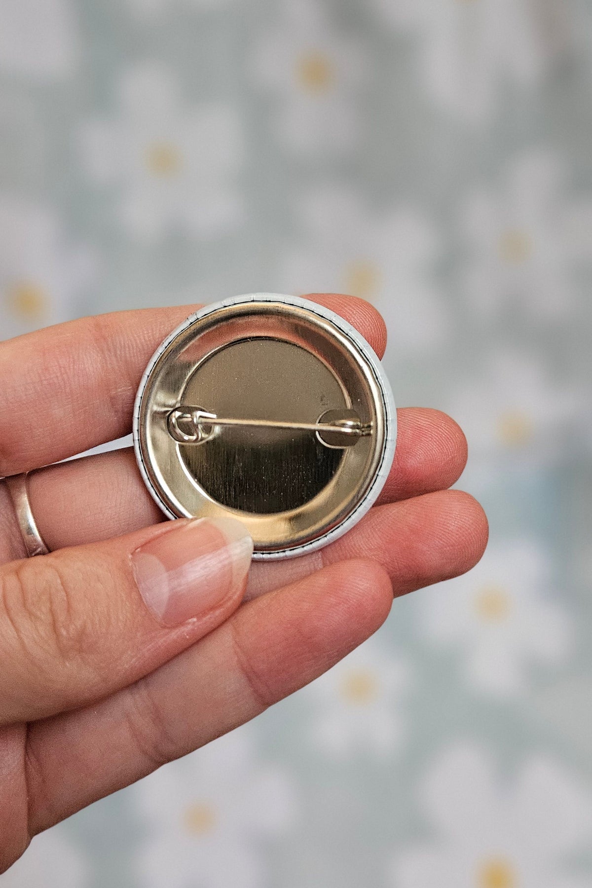Dos métallique du badge autisme de 38 mm, tenu dans une main, montrant l'épingle de fixation