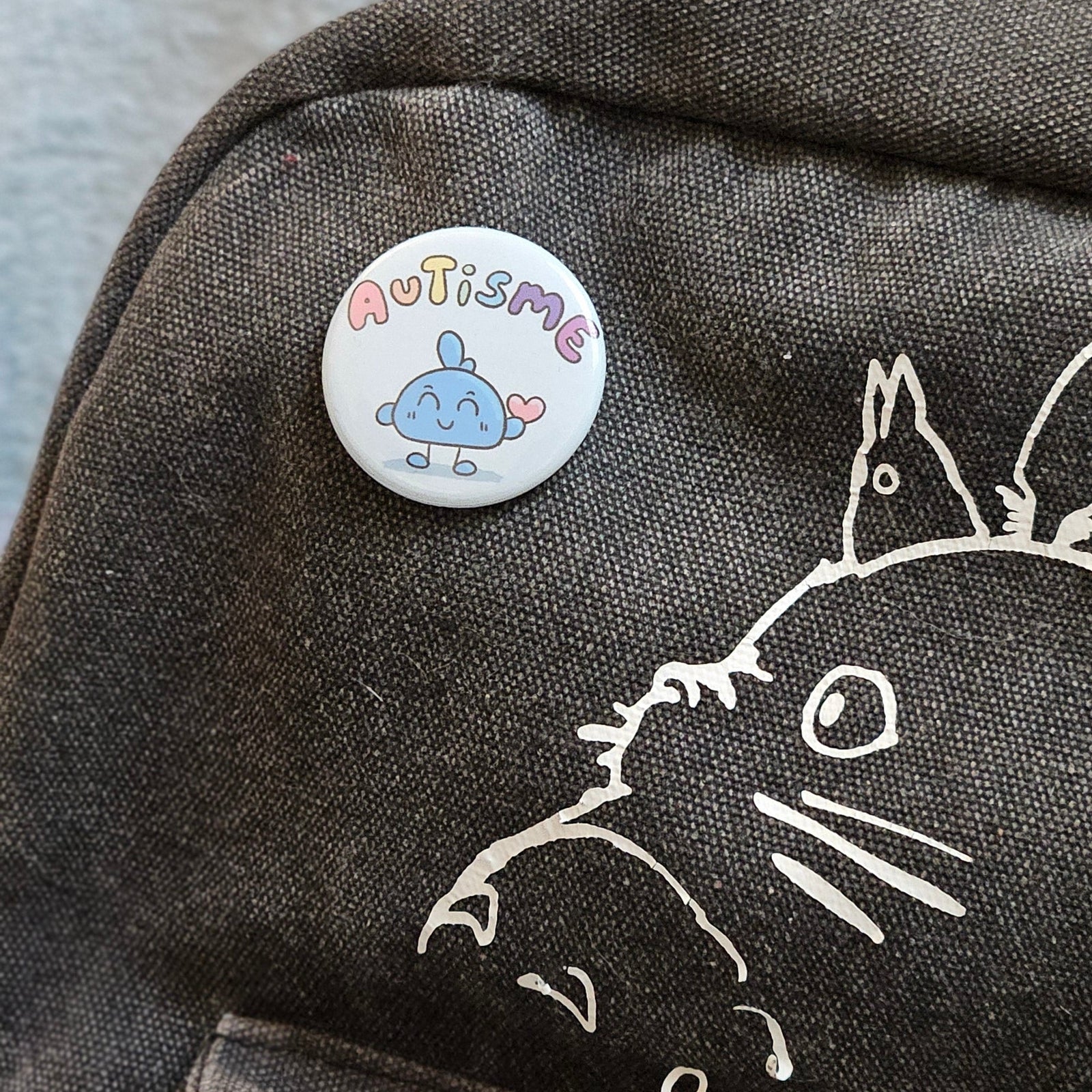 Badge autisme épinglé sur un sac à dos en toile gris foncé décoré d'un dessin au trait blanc