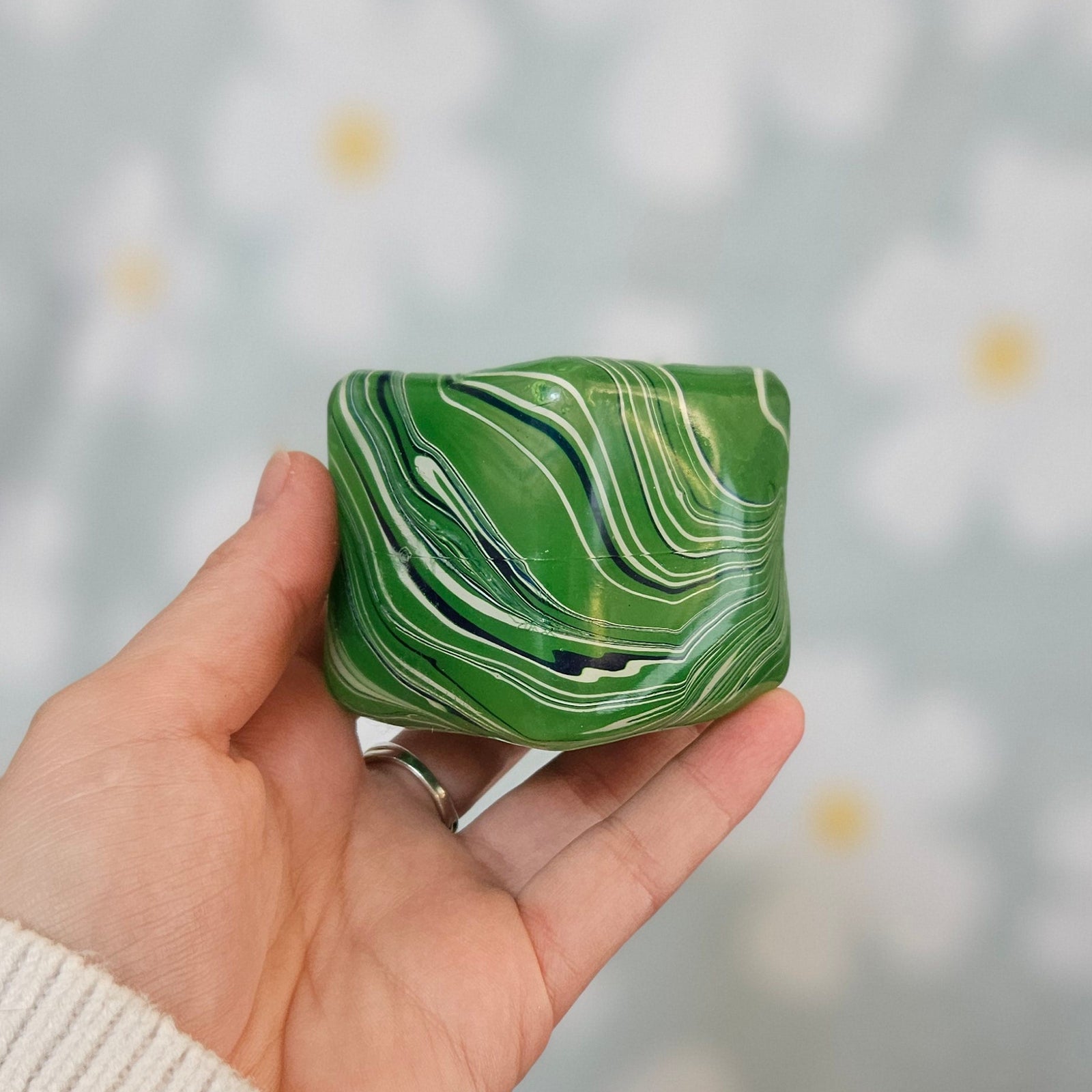 Cube squishy vert marbré de blanc et de bleu, tenu à plat dans une main