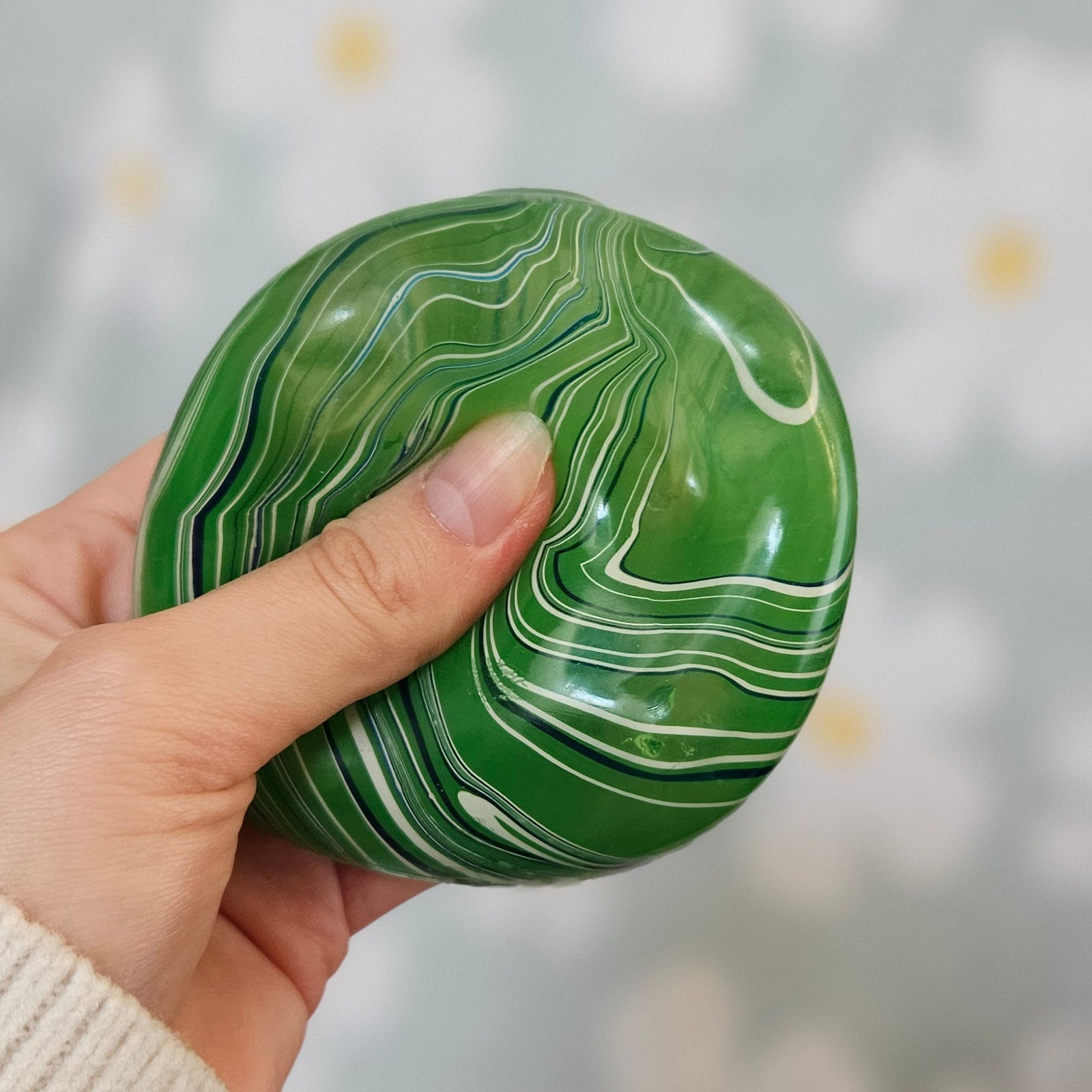 Cube squishy vert pressé entre les doigts, sa surface se déformant sous la pression du pouce