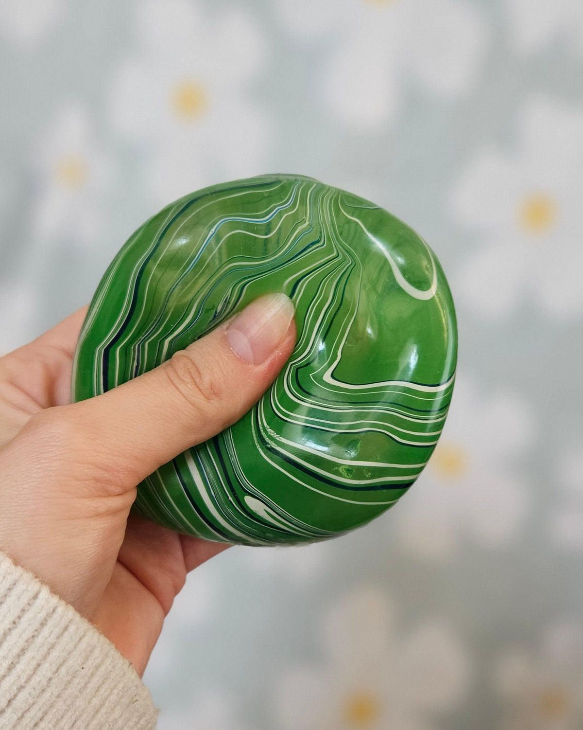 Cube squishy vert pressé entre les doigts, sa surface se déformant sous la pression du pouce