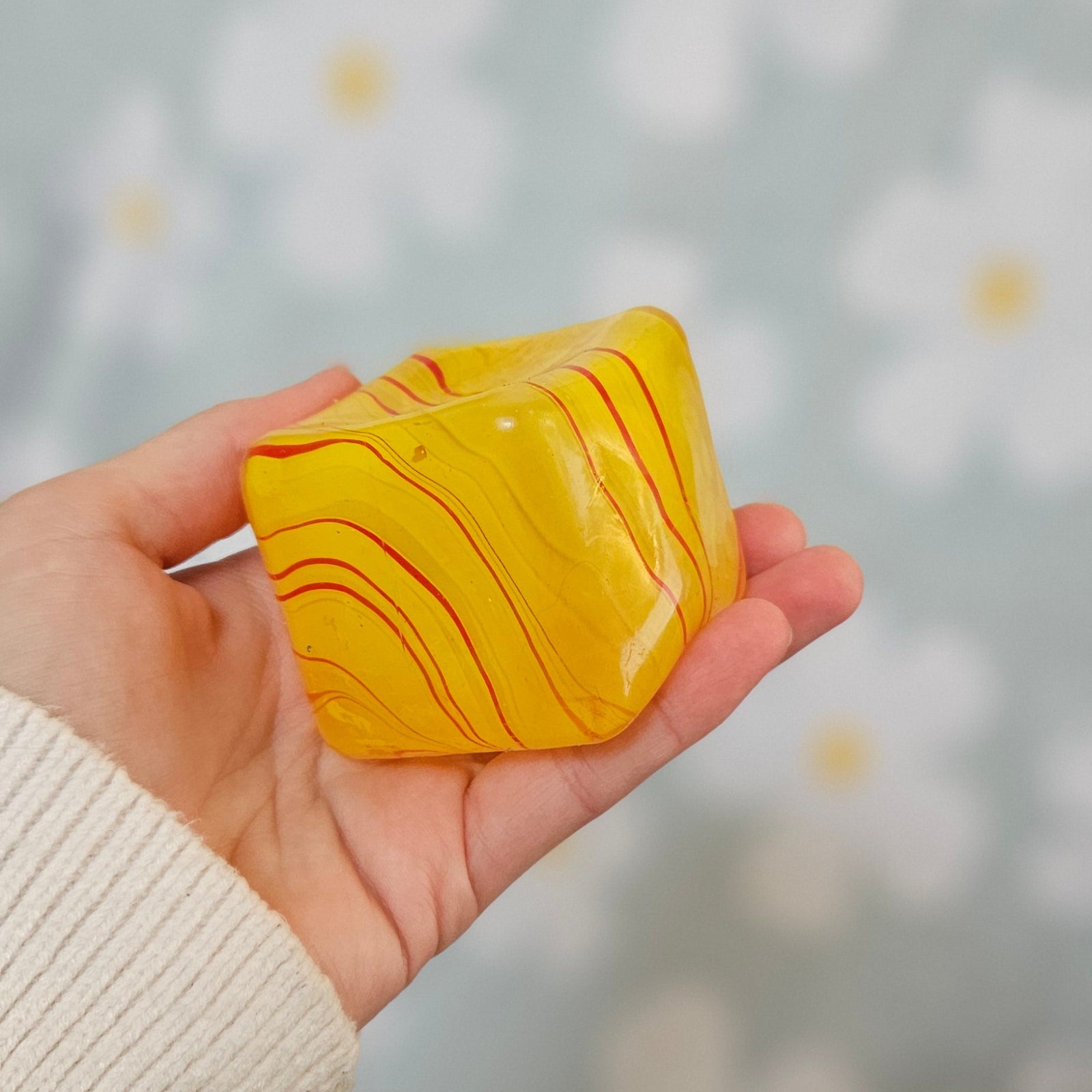 Cube squishy jaune marbré de rouge et d'orange, tenu à plat dans une main