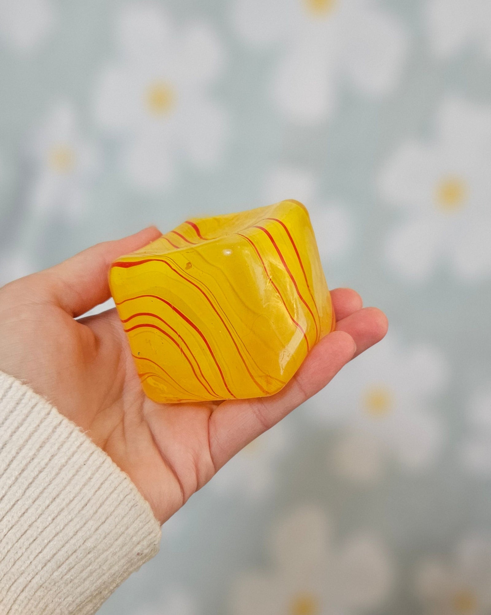 Cube squishy jaune marbré de rouge et d'orange, tenu à plat dans une main