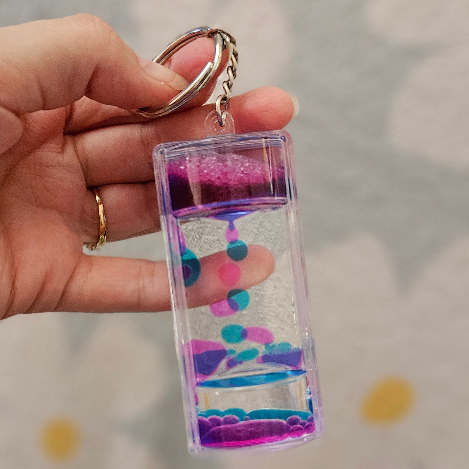Porte-clé minuteur liquide rose et bleu posé dans le creux d'une main, gouttes en cours de descente