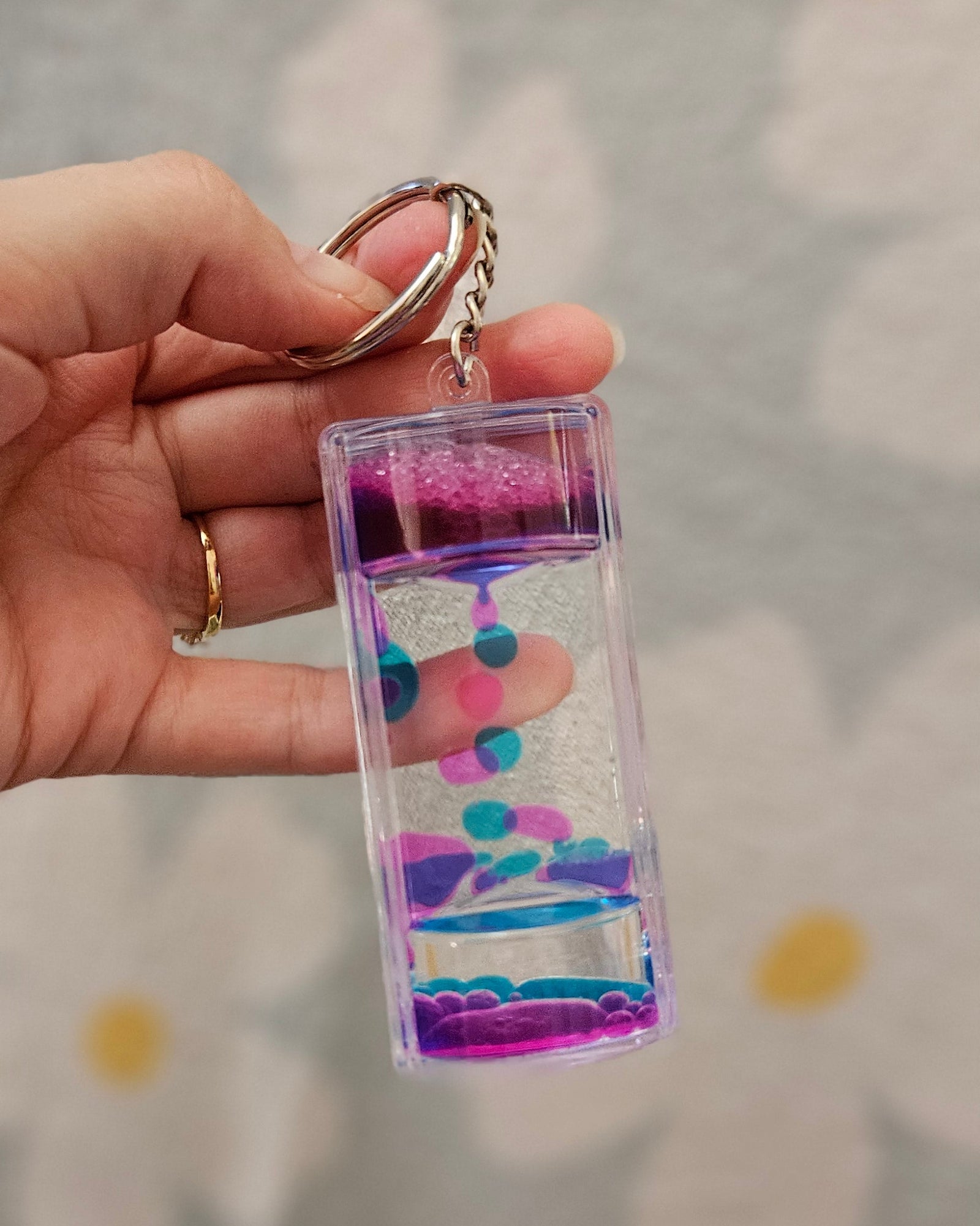 Porte-clé minuteur liquide rose et bleu posé dans le creux d'une main, gouttes en cours de descente