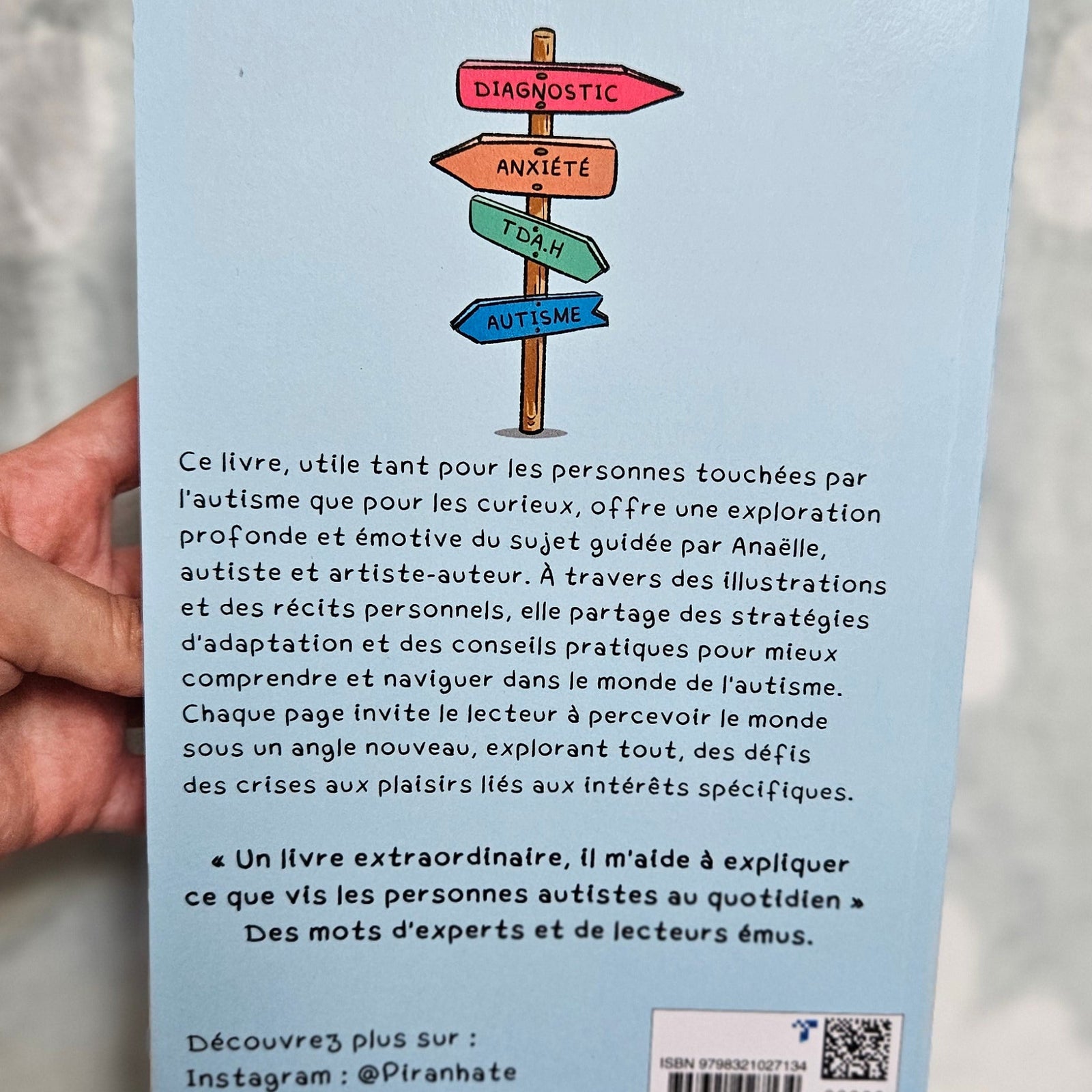 Quatrième de couverture du Guide illustré ULTIME de l'Autisme tenue en main, fond bleu clair avec un panneau indicateur et le texte de présentation du livre