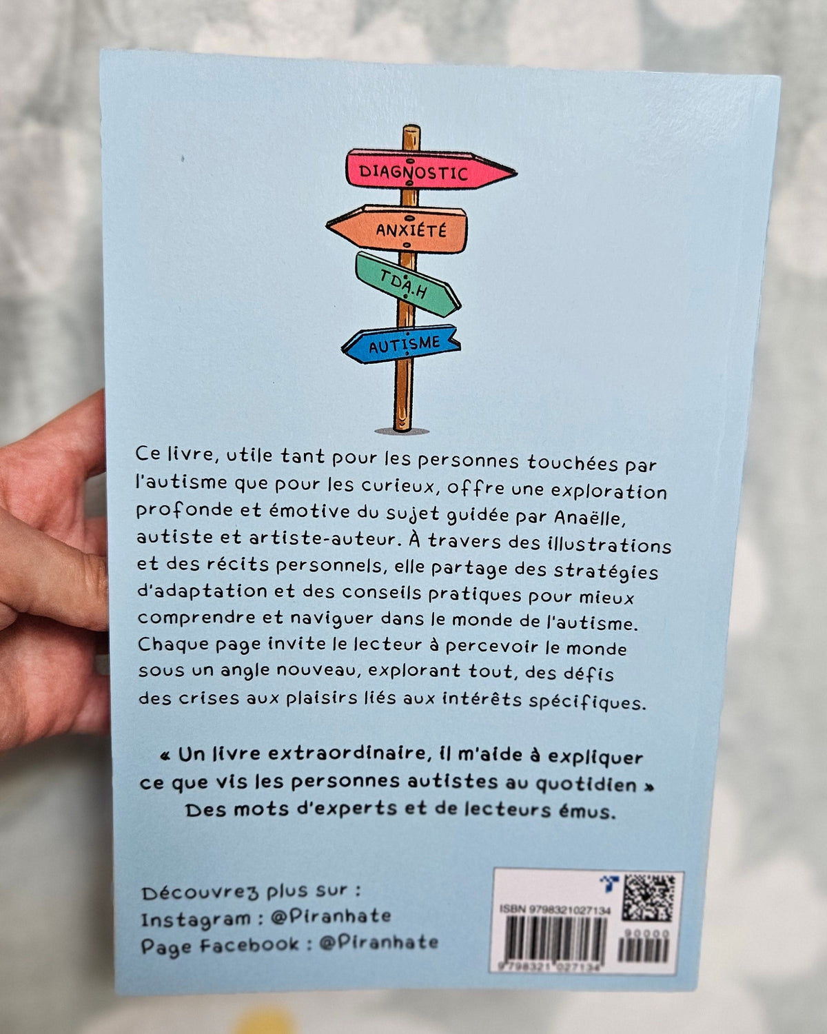Quatrième de couverture du Guide illustré ULTIME de l'Autisme tenue en main, fond bleu clair avec un panneau indicateur et le texte de présentation du livre
